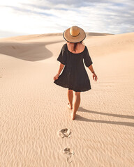 Mulher de vestido e chapéu caminhando nas dunas de areia 