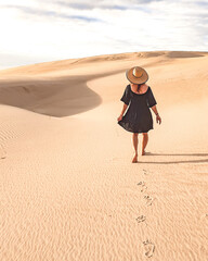 Mulher de vestido e chapéu caminhando nas dunas de areia 