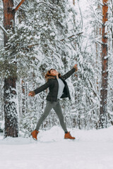 A happy girl with a short haircut bounces in the forest after a snowfall and admires the incredible nature. Christmas holidays, outdoor activities