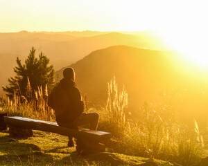 homem sentado em banco com montanhas ao fundo durante a golden hour 