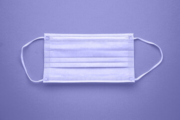 A medical disposable mask is isolated on a purple background. Tinting in the trending color of 2022. Very peri.