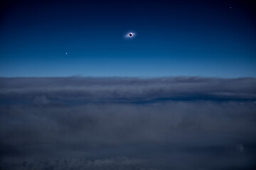 Solar eclipse on a dark blue sky above clouds and atmosphere.