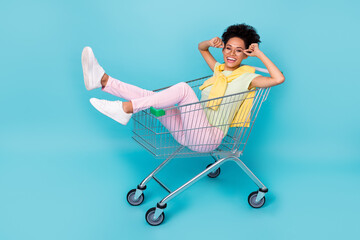 Full length profile side photo of young girl have fun sit trolley shop discount isolated over blue...