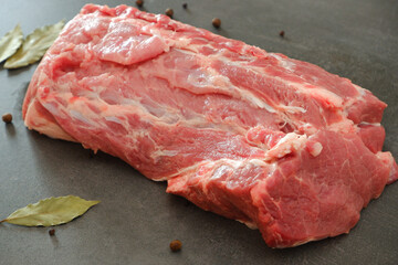 Raw meat. Uncooked fresh pork. A large juicy fresh piece of meat on a gray stone during cooking. Pepper, bay leaf. Culinary concept.