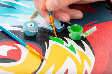 Close up on a man's hand painting. Canvas painted with numbered brushes and tempera colors. Concept of recreational activities and stimulants for the brain. Development of artistic skills.