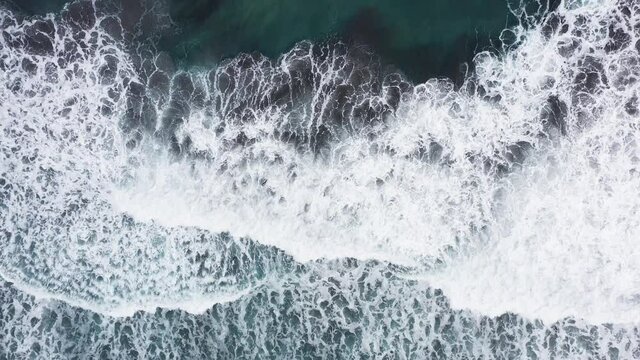 Aerial view of beautiful beach with view of ocean waves and water crashing on to sandy shore from top angle. Faroe Islands beach with waves crashing to shore. No people, epic dramatic wild beach