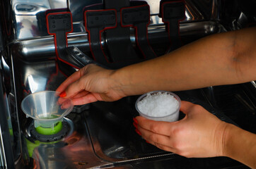 Adding salt to the dishwasher. A woman's hand pours salt to soften the water into the dishwasher....