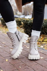 Plakat Stylish woman stands in beige shoes. Close-up of female legs in fashionable leather beige vintage boots. New seasonal collection of women's shoes