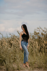 brunette girl with long hair in a black corset and blue jeans in a field