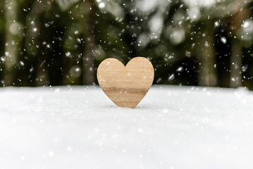 One wooden heart on the snow,blurred forest trees background.Valentine heart in winter forest, cold weather. heart symbol of romantic love, background for holiday.Copy space.
