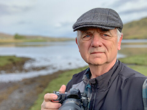 Portrait of a man wearing a flat cap standing in rural landscape taking photos, Isle of Skye, Inner Hebrides, Scotland, UK
