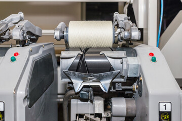 Cotton Yarn Production in a Textile Factory. Textile fabric manufacturing machines in work. Row of automated machines for yarn manufacturing. Modern Textile Plant.Selective focus.