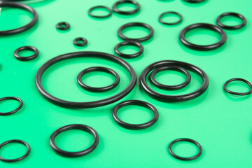 Black hydraulic and pneumatic O-rings in different sizes on a green background. Sealing gaskets for hydraulic connections. Rubber sealing rings for plumbing.