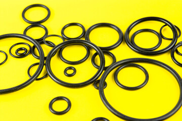 Black hydraulic and pneumatic O-rings in different sizes on a yellow background. Sealing gaskets...