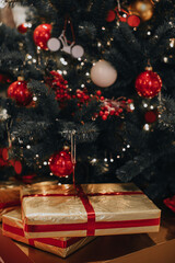 Golden New Year's gift with red ribbon under the Christmas tree. Festive holiday concept and presents