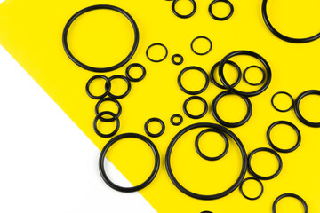 Black hydraulic and pneumatic o-rings in different sizes on a yellow and white background. Rubber...
