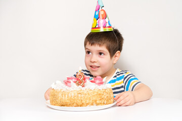 A boy celebrates his third birthday sitting at a table on a white background with a cake, looking...