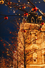 Magic Christmas postcard with golden vintage shiny european building and trees decorated with red and gold shiny Christmas balls. Evening lights