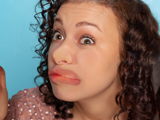 Close-up face of funny young girl crushed on glass isolated on light blue studio background.