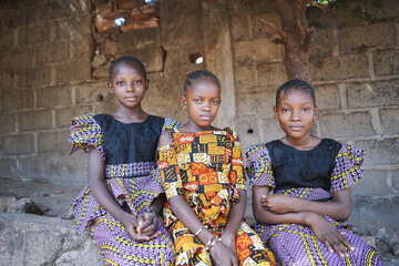 Three African girls sit together and pose in front of a brick wall