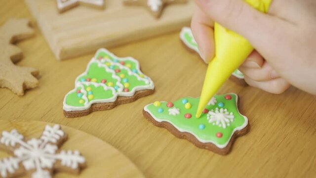 The process of decorating Christmas cookies is in motion. Close-up of a woman decorating a homemade gingerbread Christmas tree with icing sugar on the kitchen table. Home cooking