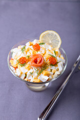 Layered salad with salted trout (salmon), caviar, eggs and vegetables. Traditional dish, one portion in a glass goblet on a gray background. Close-up.