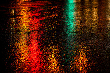 Traffic lights create a wash of color on a wet asphalt road during a rain storm.