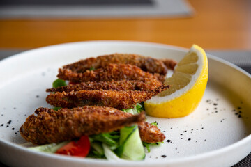 Fried smelt in a frying pan on the table with lemon and vegetables. Small sea fish