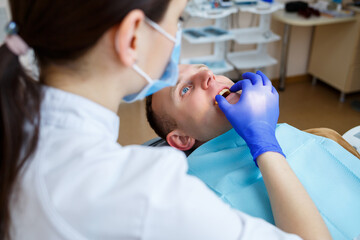 Naklejka premium Woman dentist while treating a patient. The doctor makes dental treatment on the teeth of a person in the dentist's chair. Selective focus.