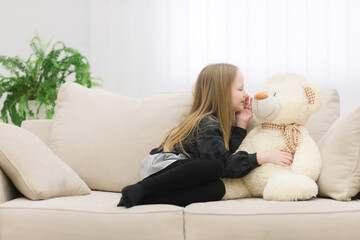 Photo of little girl sharing secrets with teddy bear on the sofa.