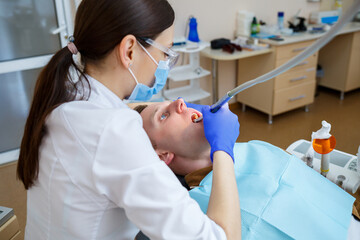 Naklejka premium Woman dentist while treating a patient. The doctor makes dental treatment on the teeth of a person in the dentist's chair. Selective focus.