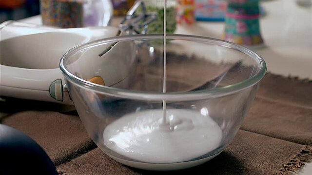 Pouring fresh cream into a glass bowl to make a tasty dessert. A hand mixer / cream whipper with other ingredients kept on the kitchen table