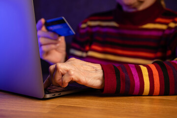 Modern elderly retired woman makes purchases online using credit card on laptop at home.