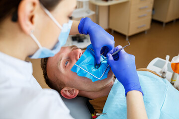 Dentist during the treatment of a male patient. Female dentist in face mask with male patient sitting in dentist chair sitting in dental clinic. Selective focus