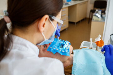Male patient sits on the dentist's chair and receives teeth restoration, female dentist at the dental clinic. Selective focus