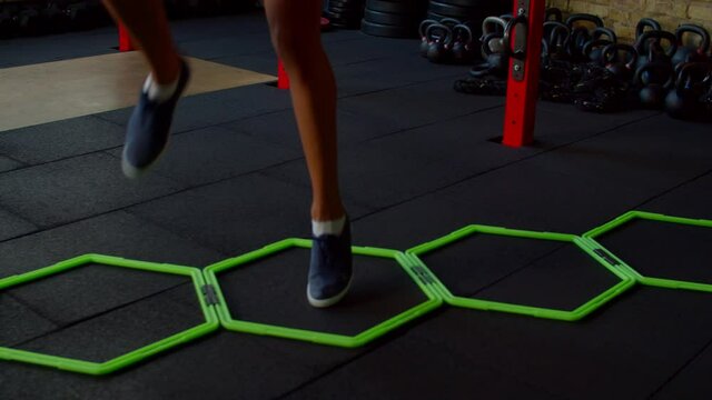 Close-up of female legs practicing cardio intense workout using hex speed rings for ability footwork training, doing high knee walking exercise, improving coordination and quickness indoors.
