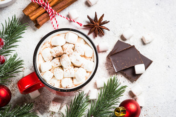 Hot chocolate with marshmallow in red mug with holiday decorations at white stone table. Top view with copy space.
