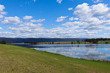 Man made rowing lake with blue sky and white clouds reflecting off almost still water surface. Mountains and trees in the background.