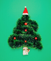 Christmas tree made of Santa´s hat, artificial garland and Santa´s sleigh. Minimal vertical flat lay composition on pastel green background, abstract Cristmass and New Year retro aesthetic decorative 