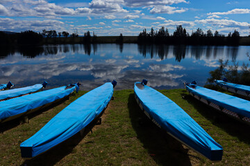 Obraz premium Line of blue rowing boats on the shoreline of the Penrith Lakes with mirror like reflection off the water