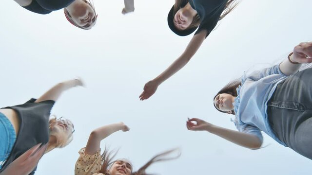 Cheerful female friends join hands against a blue sky as a sign of strong friendship.
