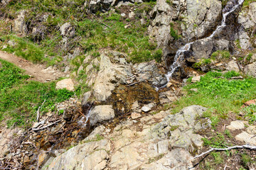 A stream on the edge of a hiking trail in the Mont Blanc massif in Europe, France, the Alps, towards Chamonix, in summer, on a sunny day.