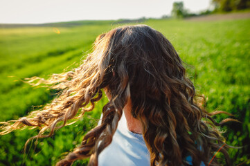 Young woman standing on street with hair blown by the wind, covering her face. Young casual girl with wavy hair. Dark-haired  woman with messy windy tousy blowsy hair, long wavy hair fly in the wind