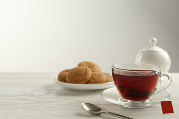 Tea bag in glass cup of hot water on white wooden table. Space for text