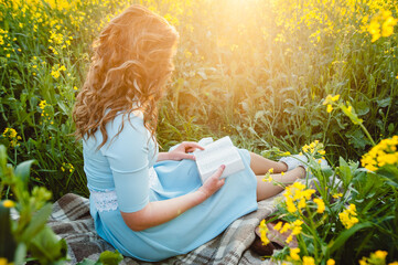 A girl sits in a field on a lawn of yellow flowers, reading a book on a summer sunny day. A...