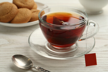 Tea bag in glass cup of hot water on white wooden table, closeup