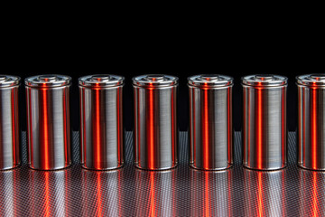 A consignment of new modern high-capacity lithium-ion cells. A prototype of new batteries on a steel surface illuminated with red light on a black background