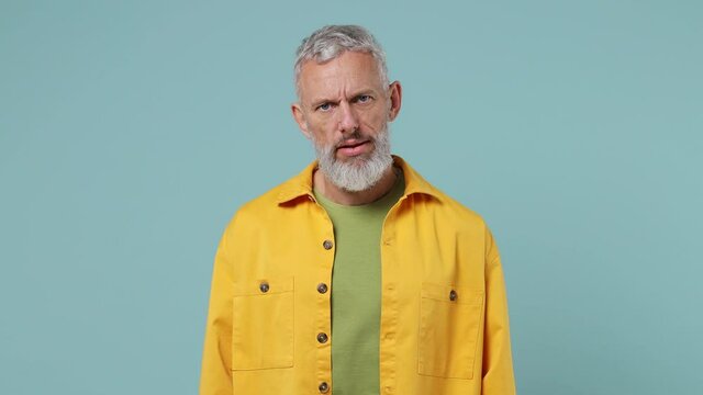 Displeased irritated sad angry elderly gray-haired bearded man 50s wears yellow shirt closed eyes cover ears do not want to listen scream isolated on plain pastel light blue background studio portrait