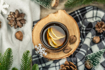 Fototapeta na wymiar Hot black tea and lemon with winter decor. Cozy sweater, fir tree branches, nuts, snowflakes