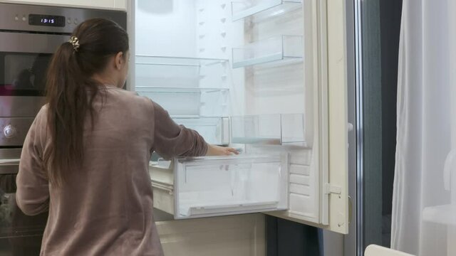 New modern white kitchen, woman cleaning empty integrated refrigerator built into kitchen housing. High quality 4k footage